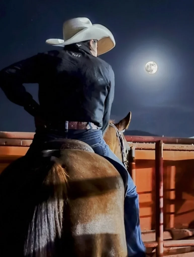 una barrilera montada sobre su caballo en una noche de luna llena donde nos dan la espalda y su blusa negra solo se refleja el pequeño bordado característico de tret